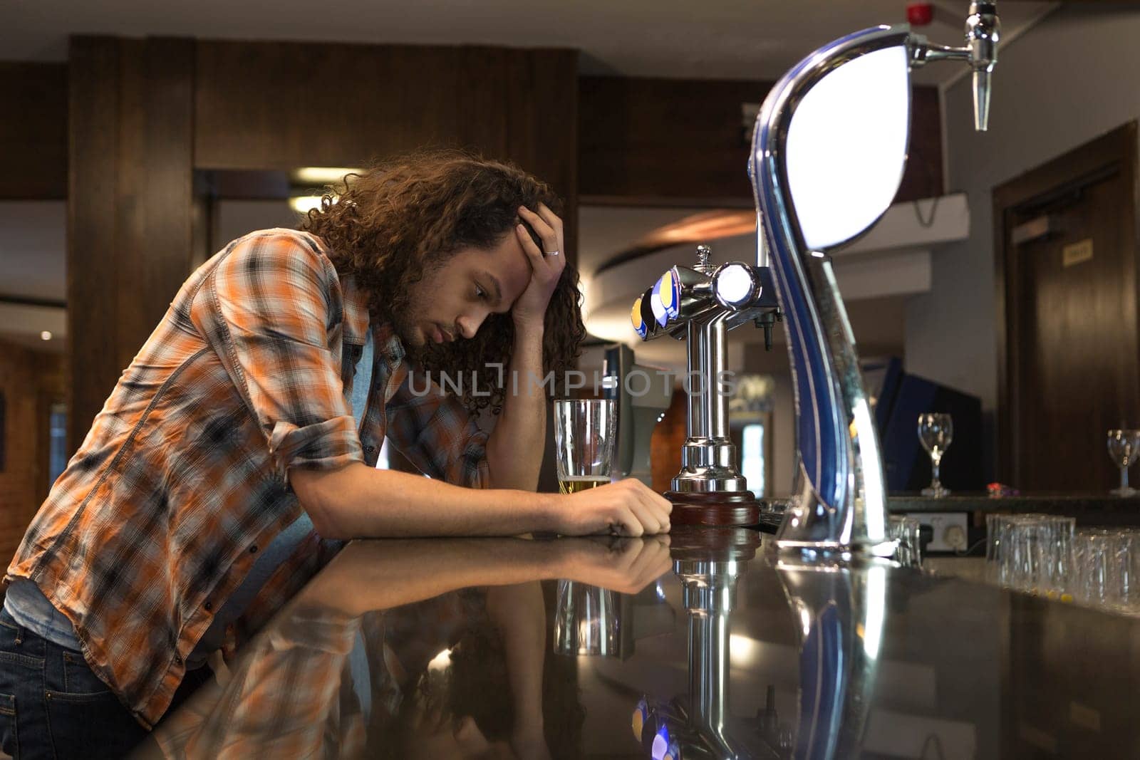 Man standing at a bar looking very stressed with his head in his hand.