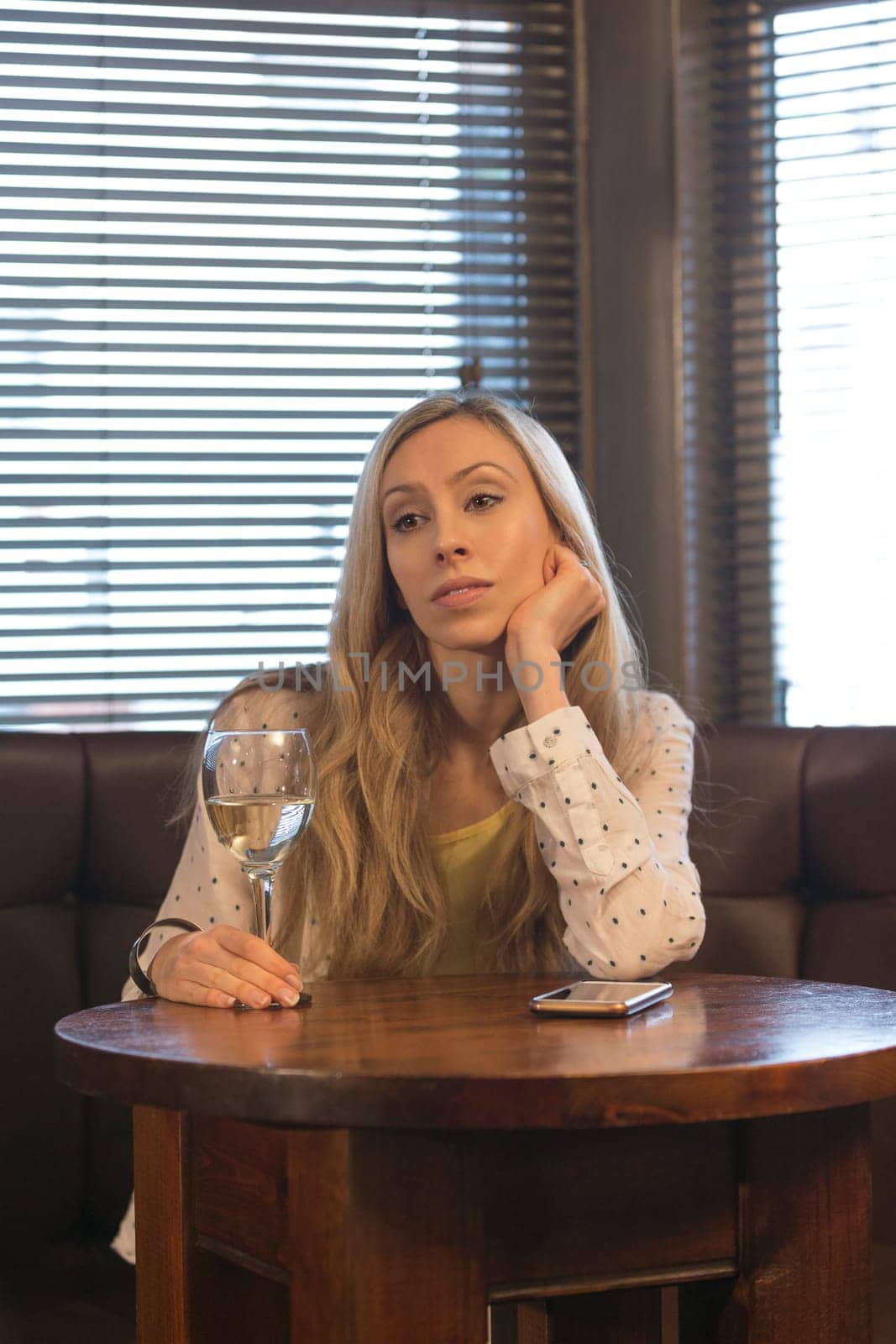 Young woman sitting on her own in a bar with a glass of wine and a smartphone.