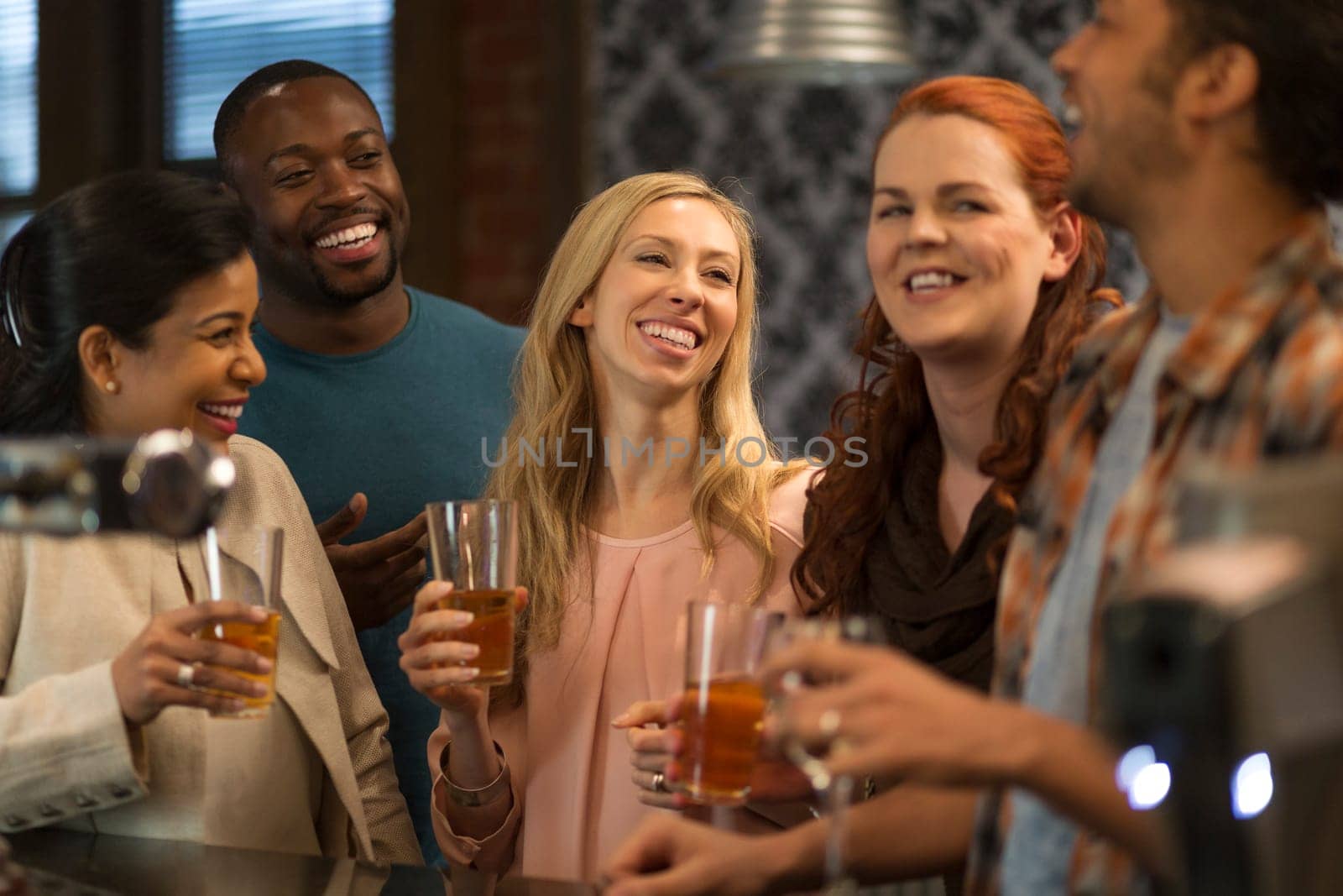 Group of friends drinking beer at a bar. They are all laughing and talking to eachother.