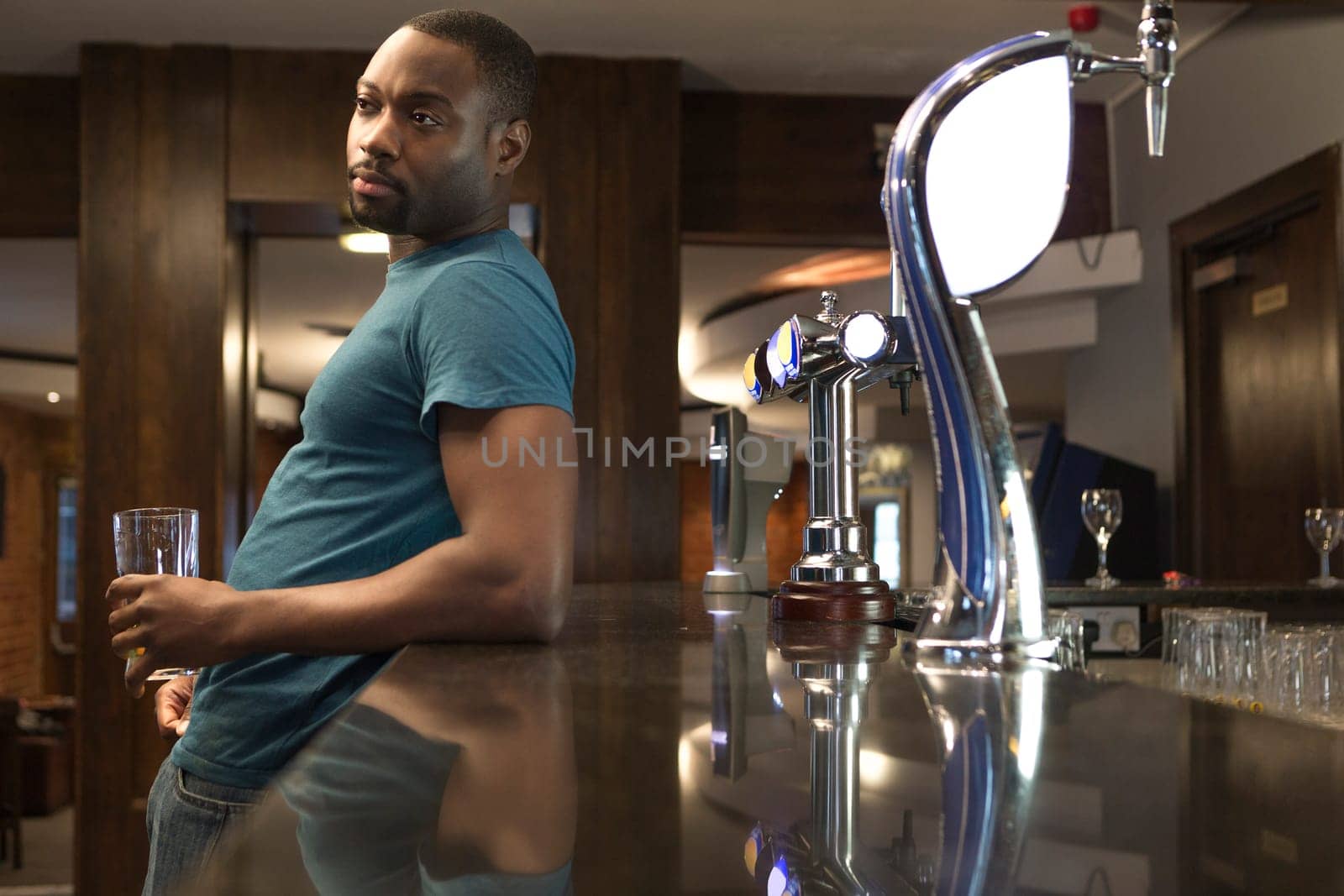 Young man standing at the bar looking deep in thought, with a pint in his hand.
