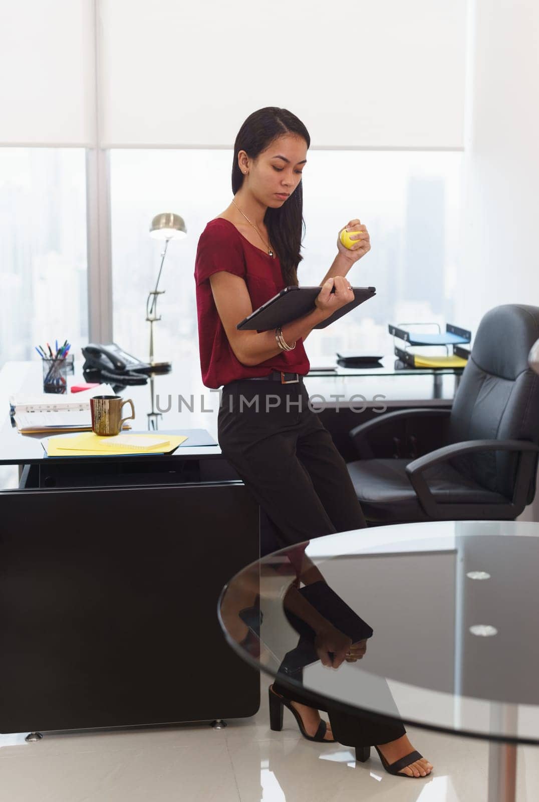 Office worker leaning on desk. The woman reads an email on tablet computer and holds an anti-stress yellow ball. She feels stressed and nervous