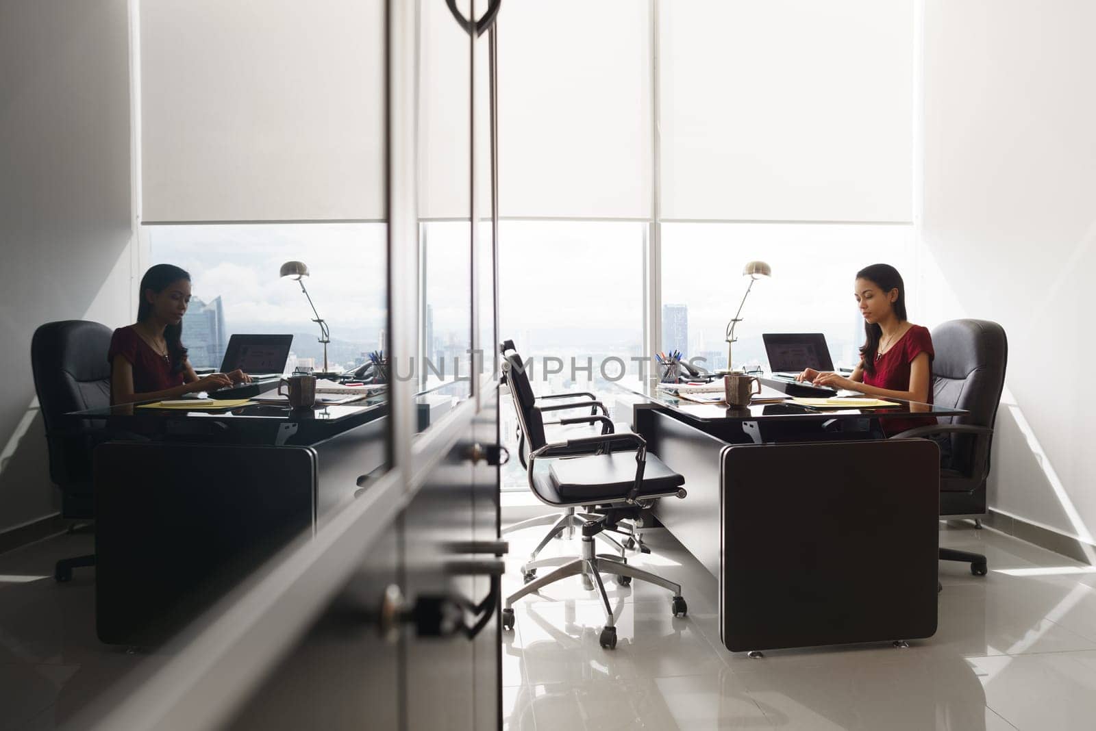 Adult businesswoman sitting in modern office in skyscraper. The secretary is concentrated and writes email on tablet computer. Wide shot