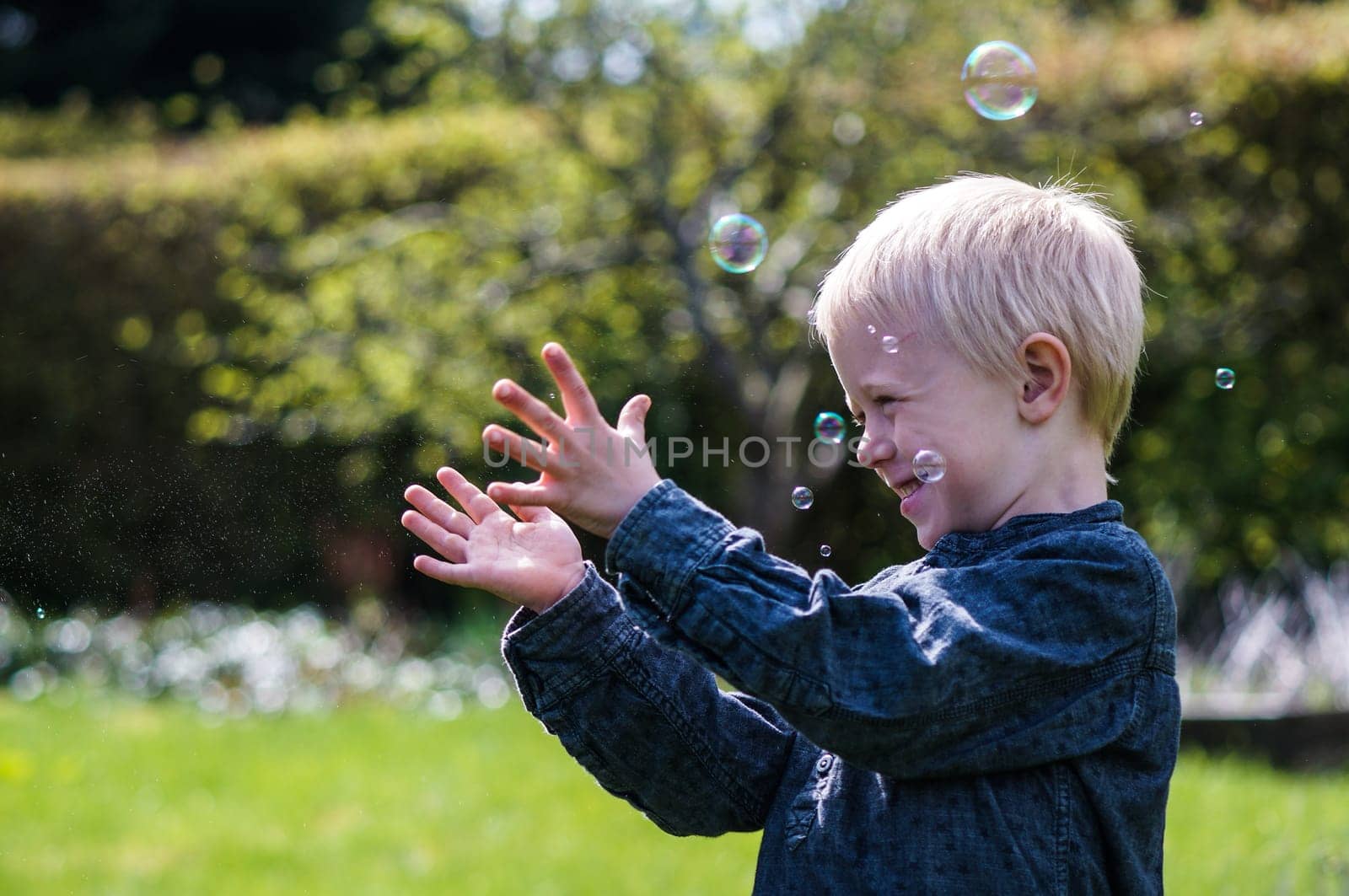 A Little boy blows soap bubbles in the garden on a summer day. He wears a blue shirt and is happy