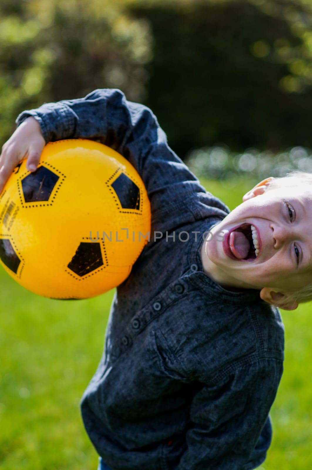 Preschool Child with Football, soccer ball. Boy that's out in the garden with his football . His football is yellow. He wears a blue shirt . It's summer and good weather and the boy is happy