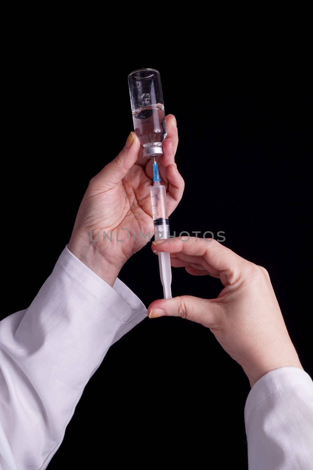 Filling of a syringe with medicine from vial. Medical person holding medical syringe and drug vial. Tip of needle shows. Isolated Black background.