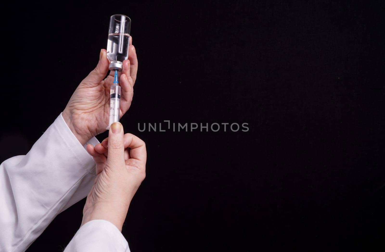 Filling of a syringe with medicine from vial. Medical person holding medical syringe and drug vial. Tip of needle shows. Isolated Black background.
