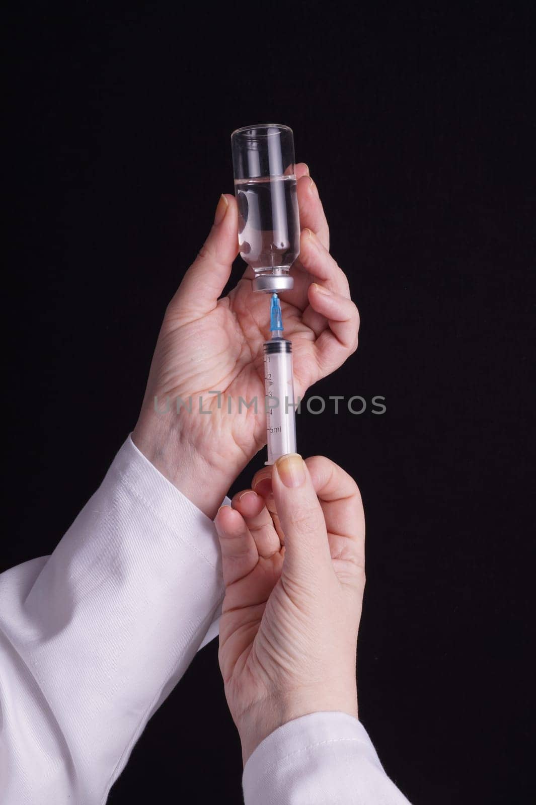 Filling of a syringe with medicine from vial. Medical person holding medical syringe and drug vial. Tip of needle shows. Isolated Black background.