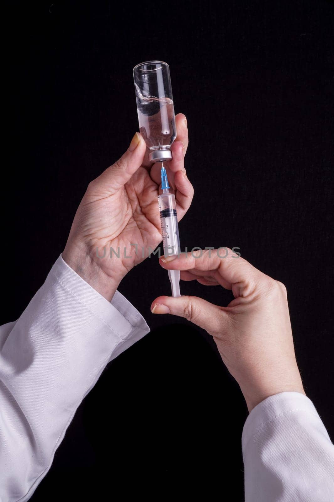 Filling of a syringe with medicine from vial. Medical person holding medical syringe and drug vial. Tip of needle shows. Isolated Black background.