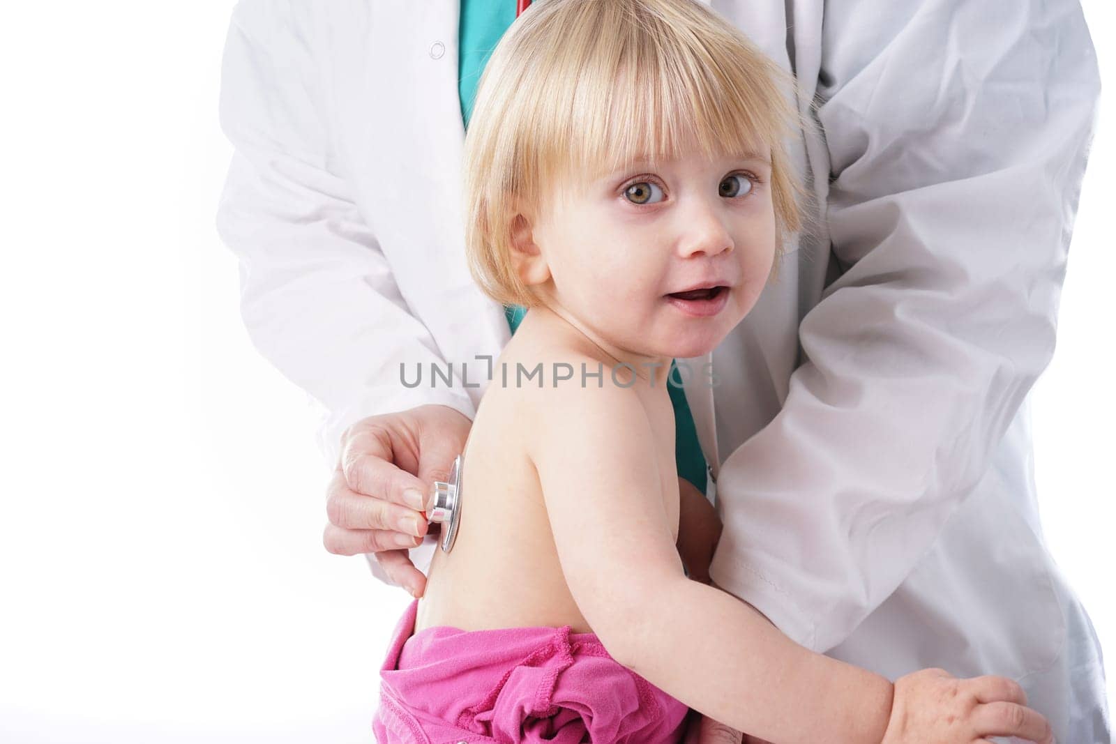 The doctor examines toddler child and listening to heart and lungs with stethoscope. The baby girl is happy, isolated on white