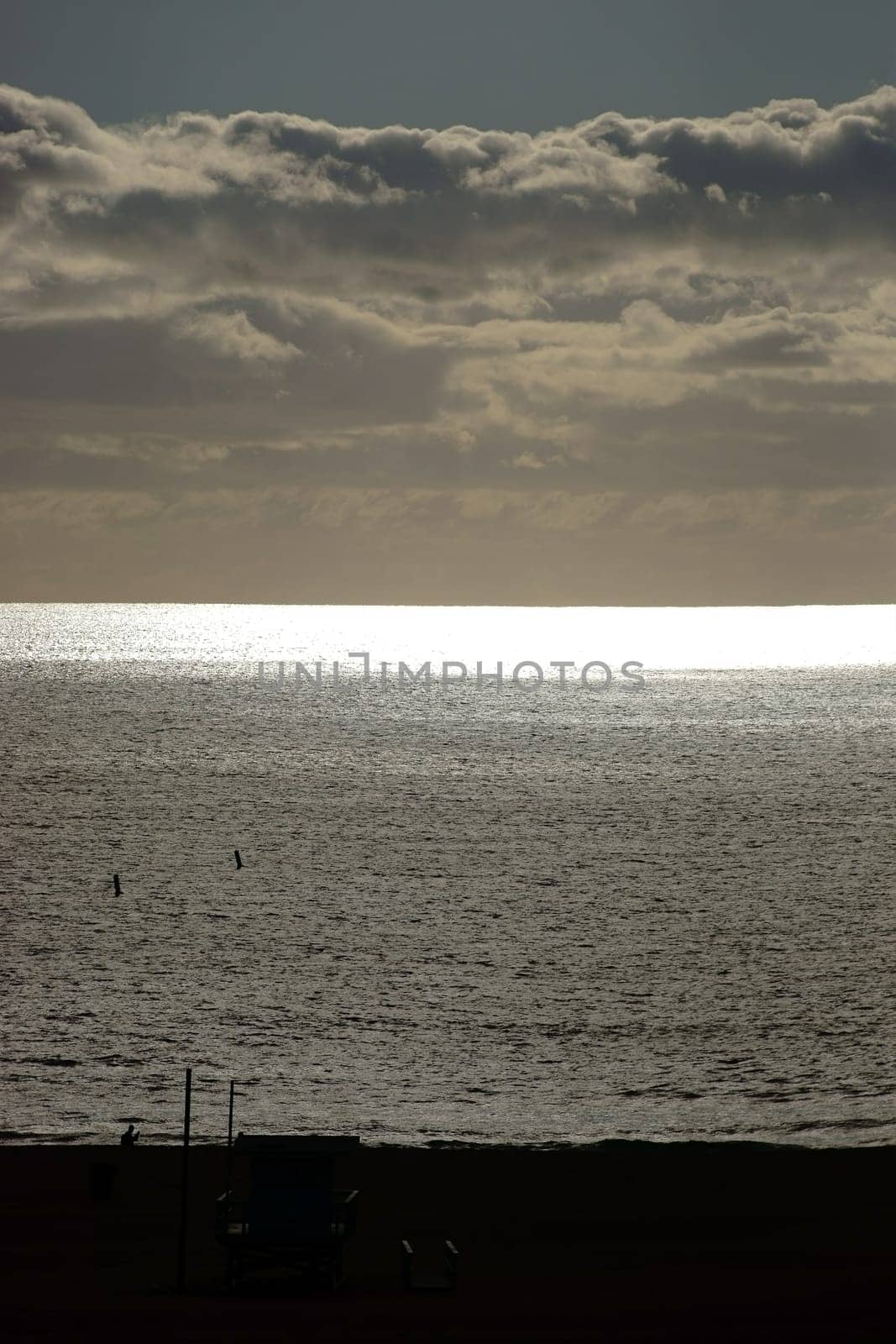 The silhouette of a jogger and a guardhouse in the evening on the beach with sun reflections in the water.