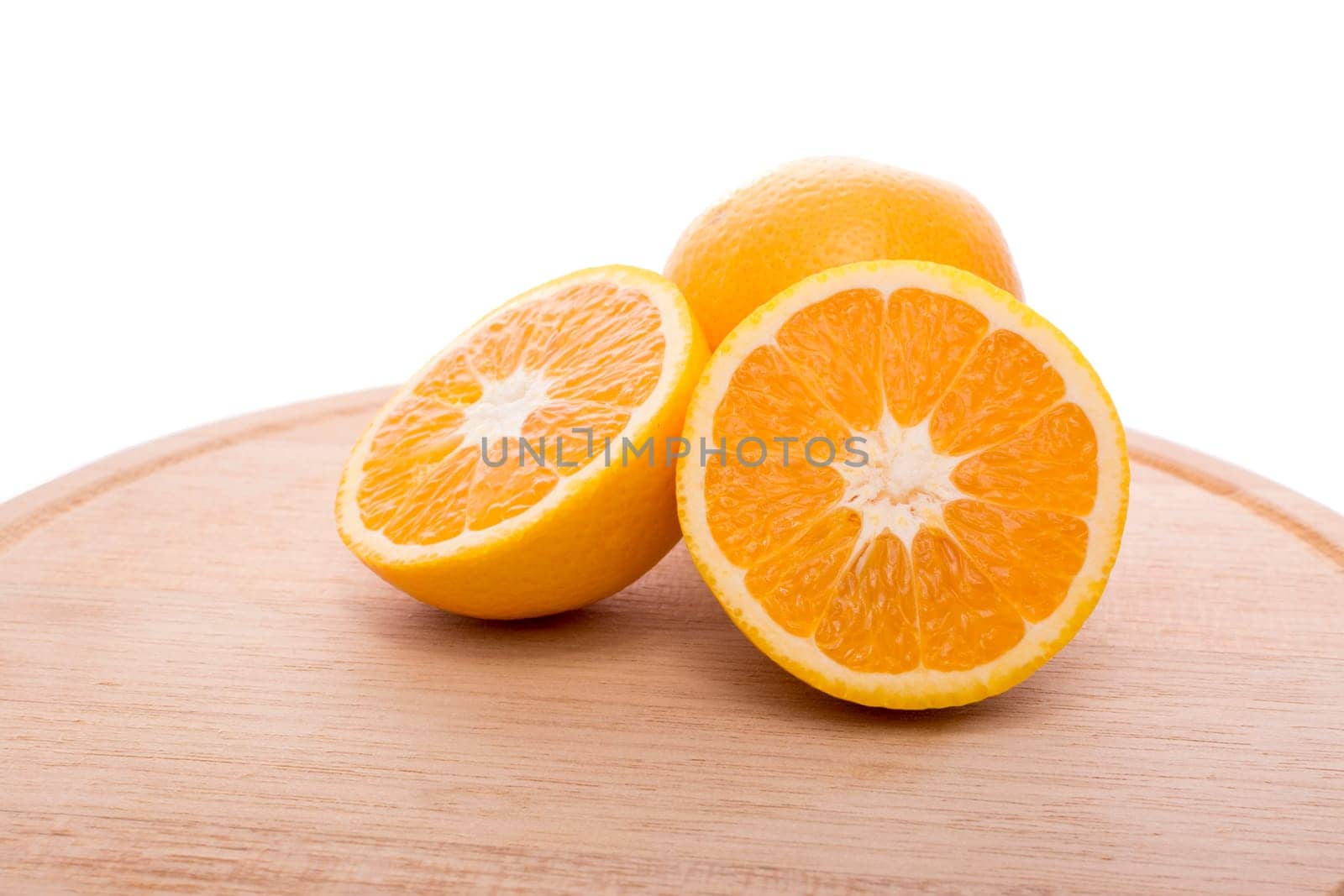 Approach and presentation of an orange split in half and a full in the back. They are on a wooden plate and white background