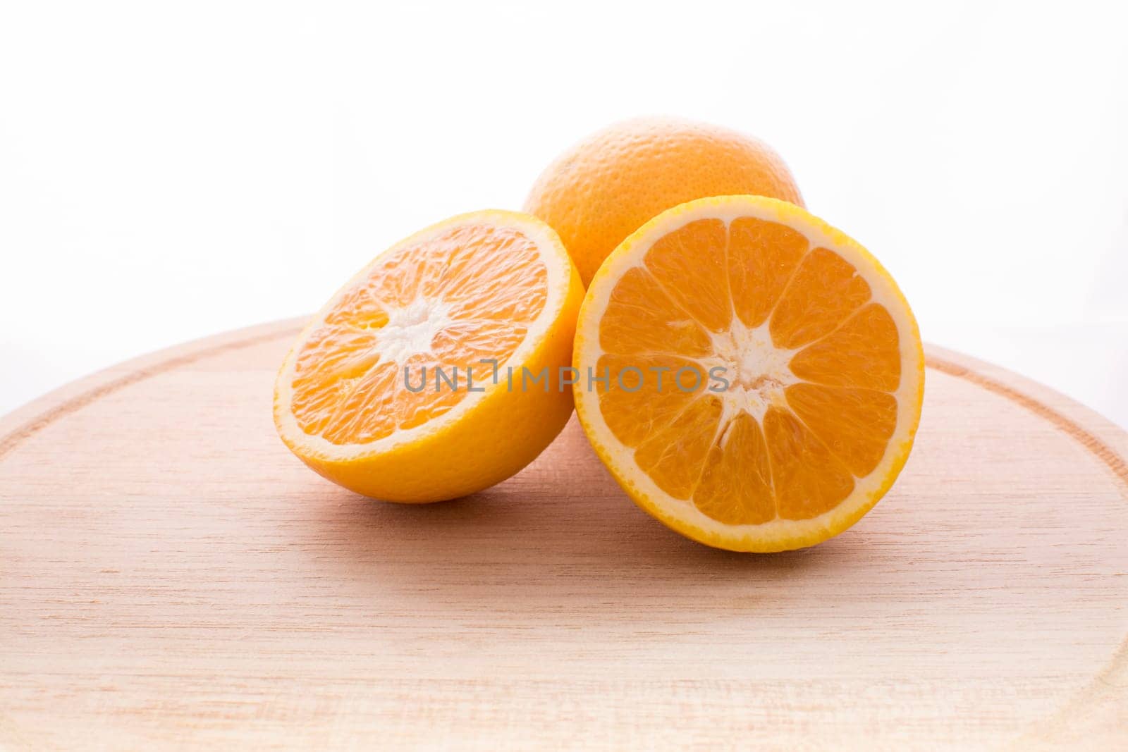 Approach and presentation of an orange split in half and a full in the back. They are on a wooden plate and white background