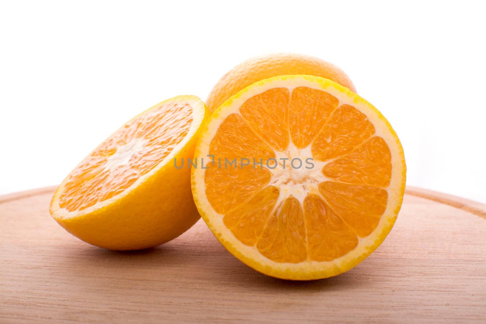 Approach and presentation of an orange split in half and a full in the back. They are on a wooden plate and white background