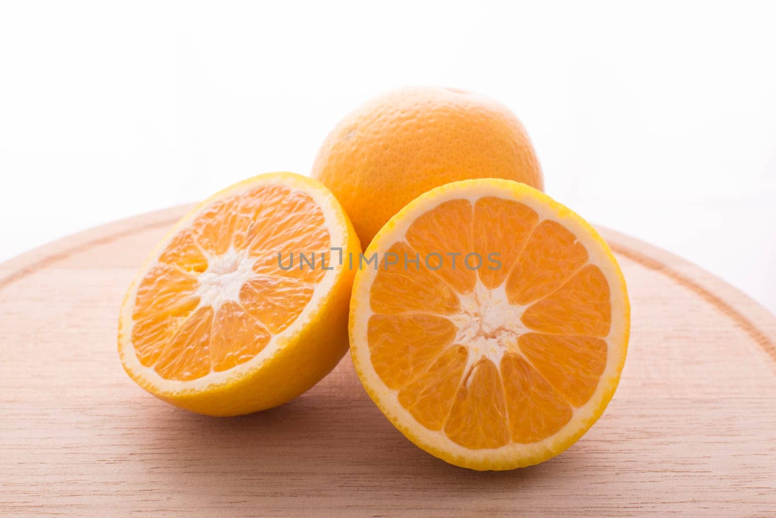 Approach and presentation of an orange split in half and a full in the back. They are on a wooden plate and white background