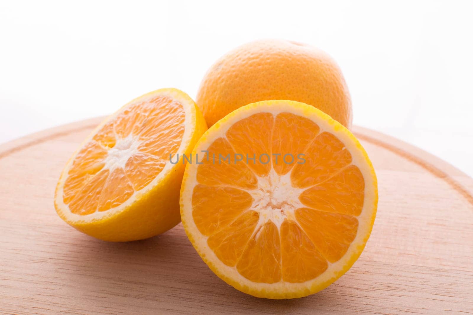 Approach and presentation of an orange split in half and a full in the back. They are on a wooden plate and white background
