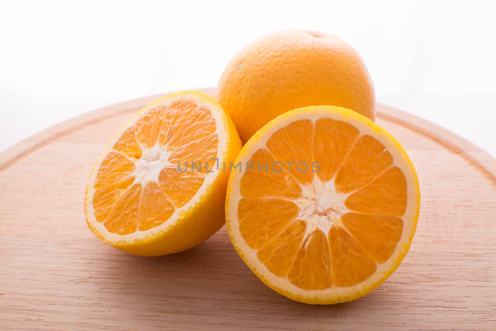 Approach and presentation of an orange split in half and a full in the back. They are on a wooden plate and white background