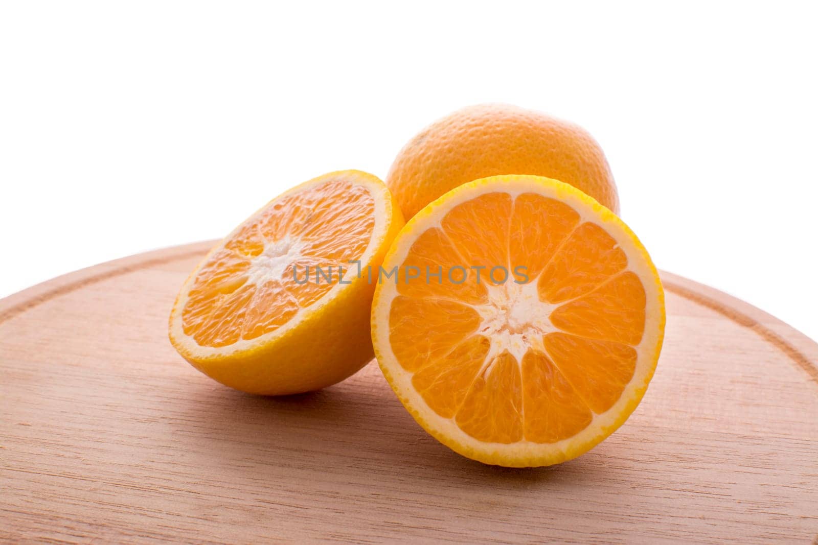 Approach and presentation of an orange split in half and a full in the back. They are on a wooden plate and white background