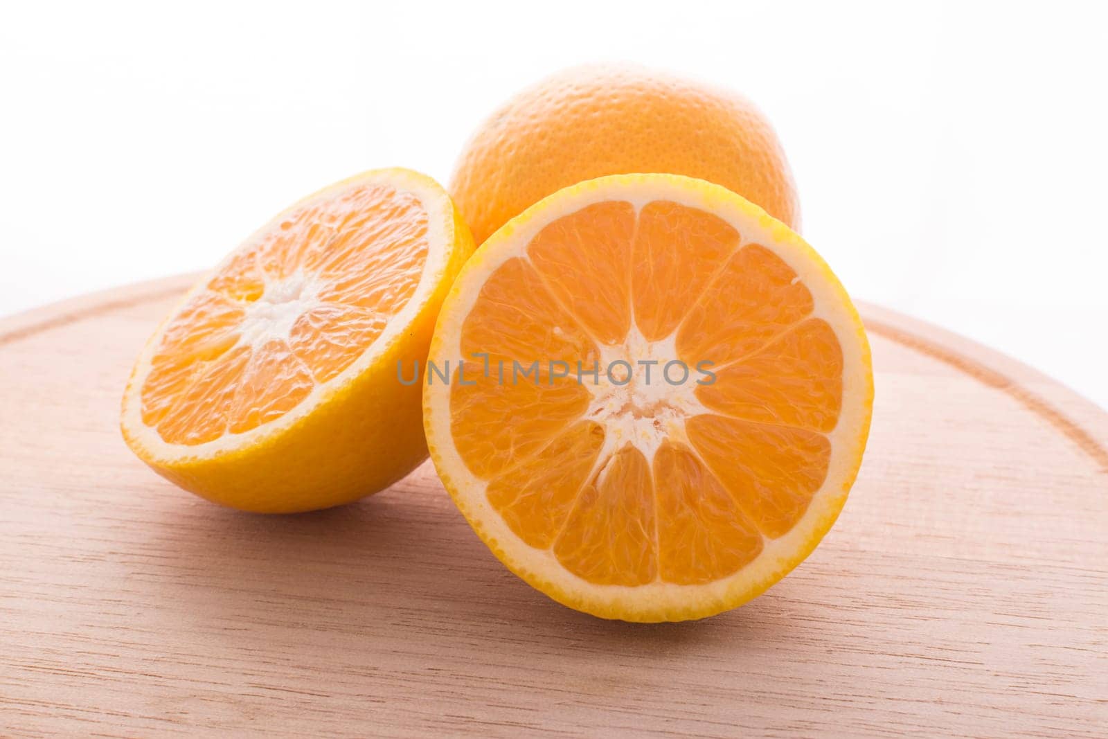 Approach and presentation of an orange split in half and a full in the back. They are on a wooden plate and white background