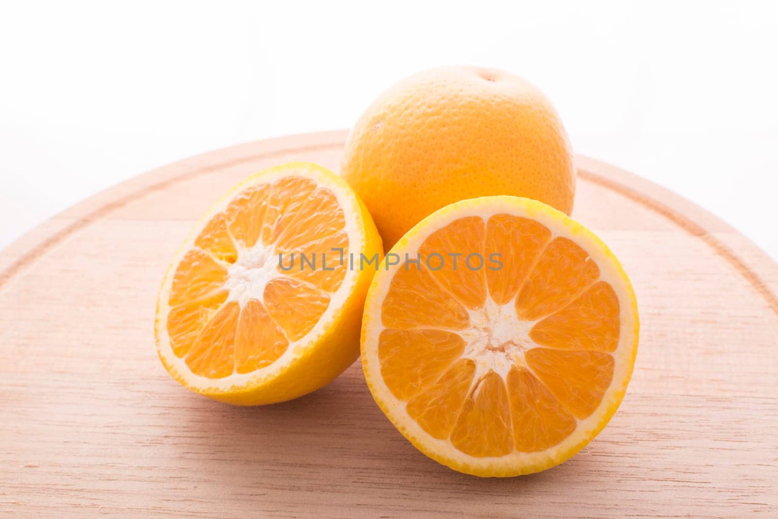 Approach and presentation of an orange split in half and a full in the back. They are on a wooden plate and white background