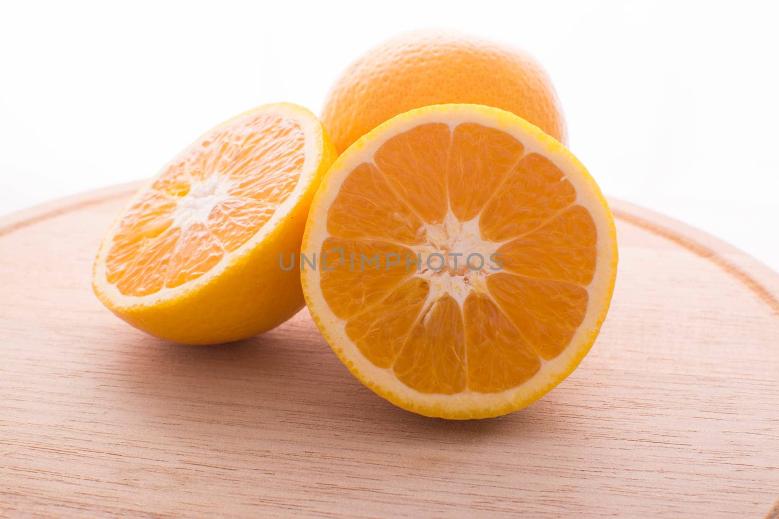 Approach and presentation of an orange split in half and a full in the back. They are on a wooden plate and white background