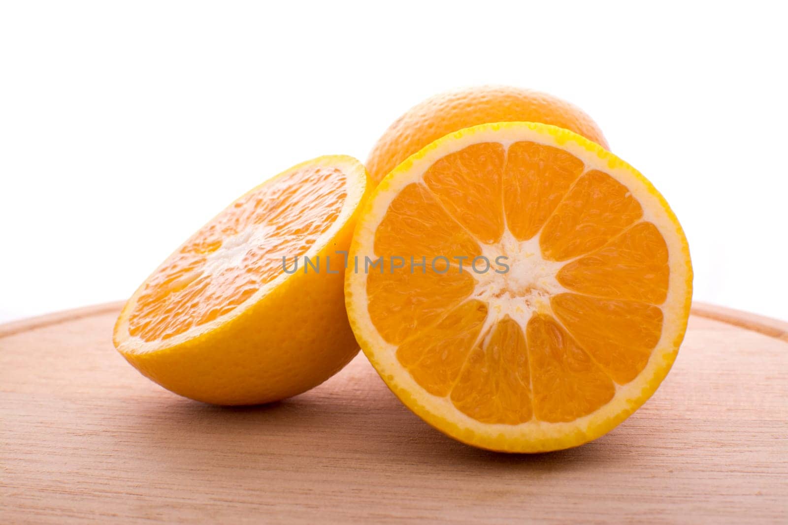Approach and presentation of an orange split in half and a full in the back. They are on a wooden plate and white background