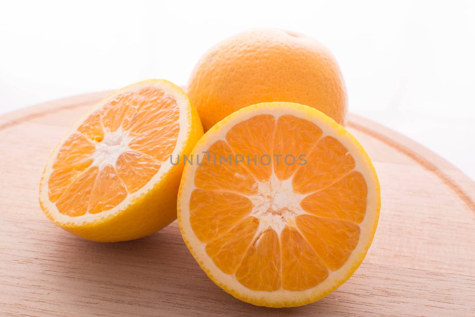 Approach and presentation of an orange split in half and a full in the back. They are on a wooden plate and white background