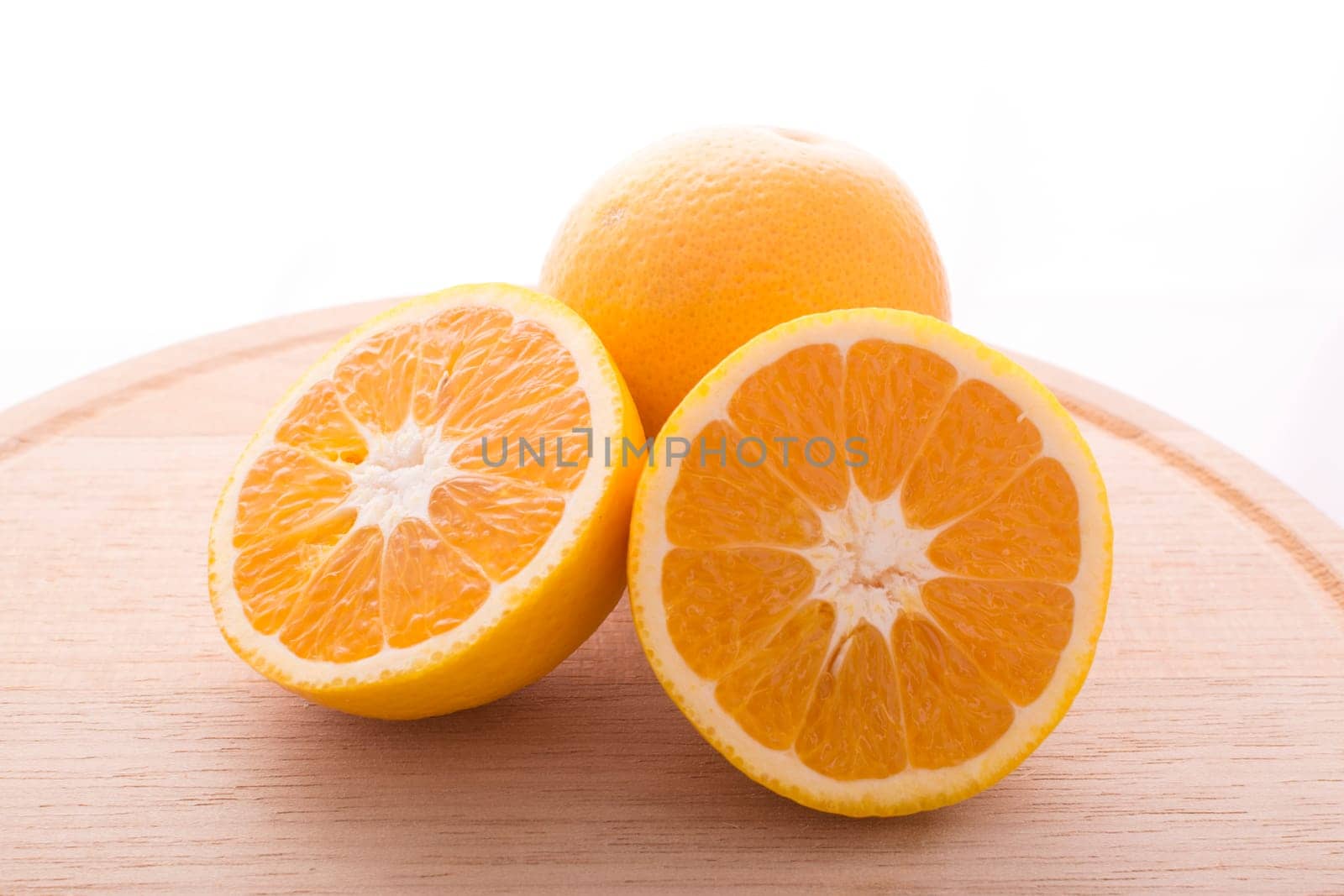Approach and presentation of an orange split in half and a full in the back. They are on a wooden plate and white background