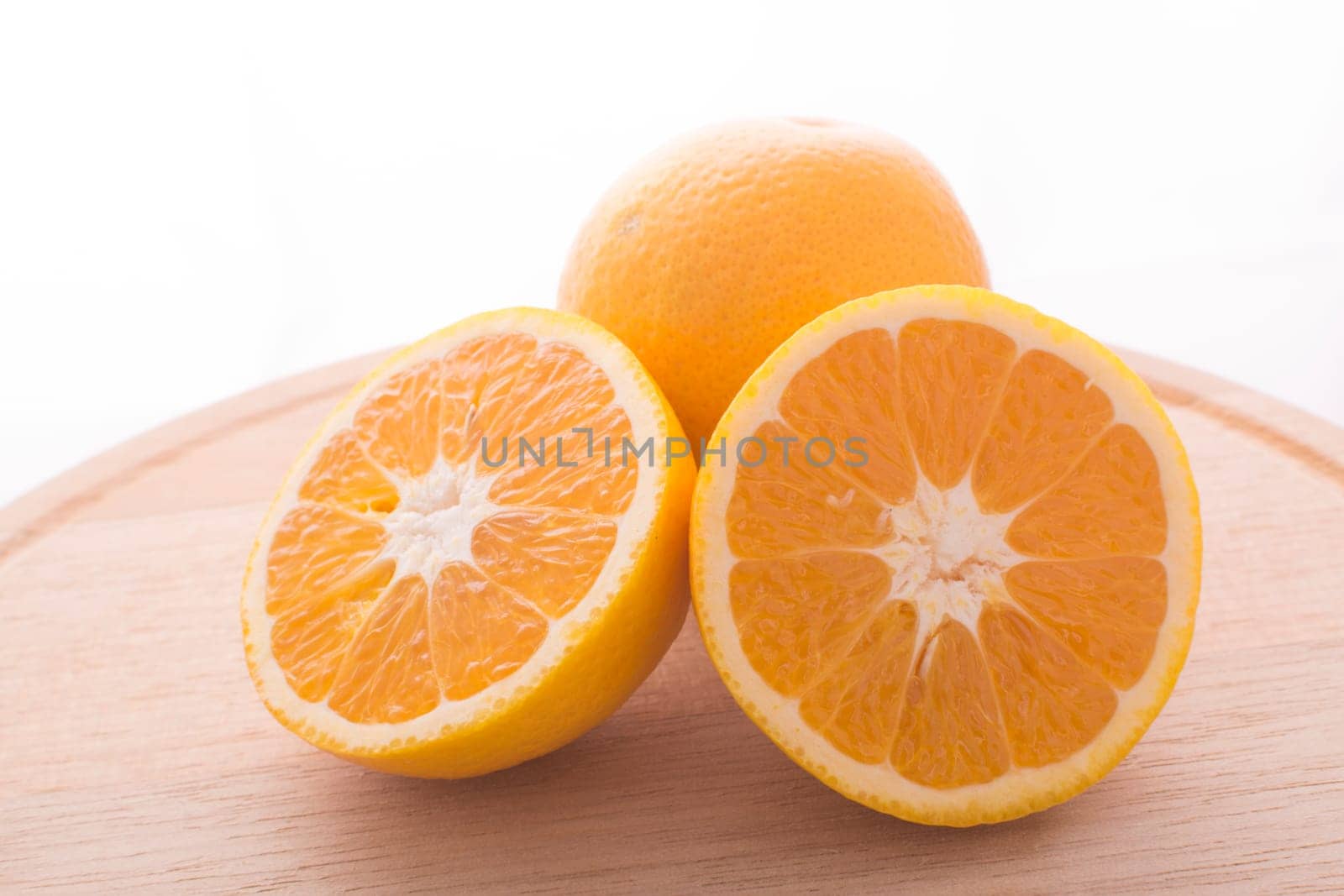 Approach and presentation of an orange split in half and a full in the back. They are on a wooden plate and white background