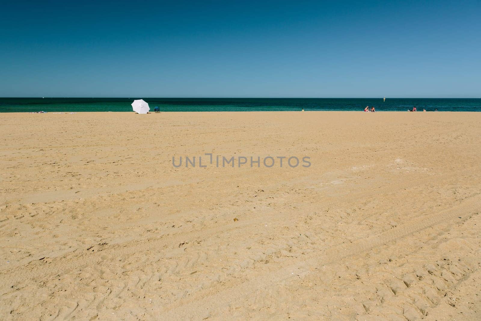Mordialloc Beach in Melbourne. A large white umbrella near the waterline shelters its occupants.