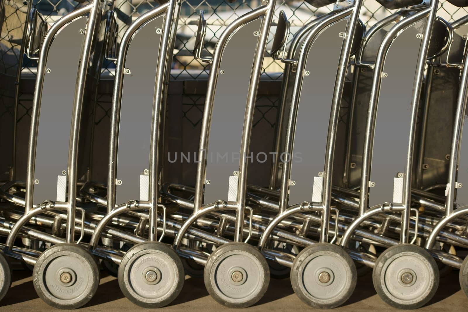 Luggage trolleys of a luggage cart rental stand one after the other at the sidewalk and entrance of an airport.