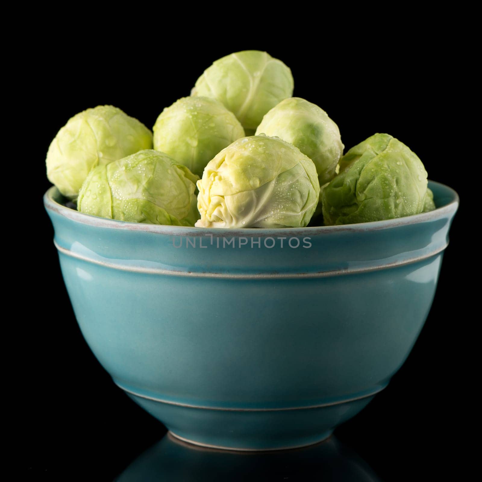 Fresh brussels sprouts on blue ceramic bowl isolated on black background.