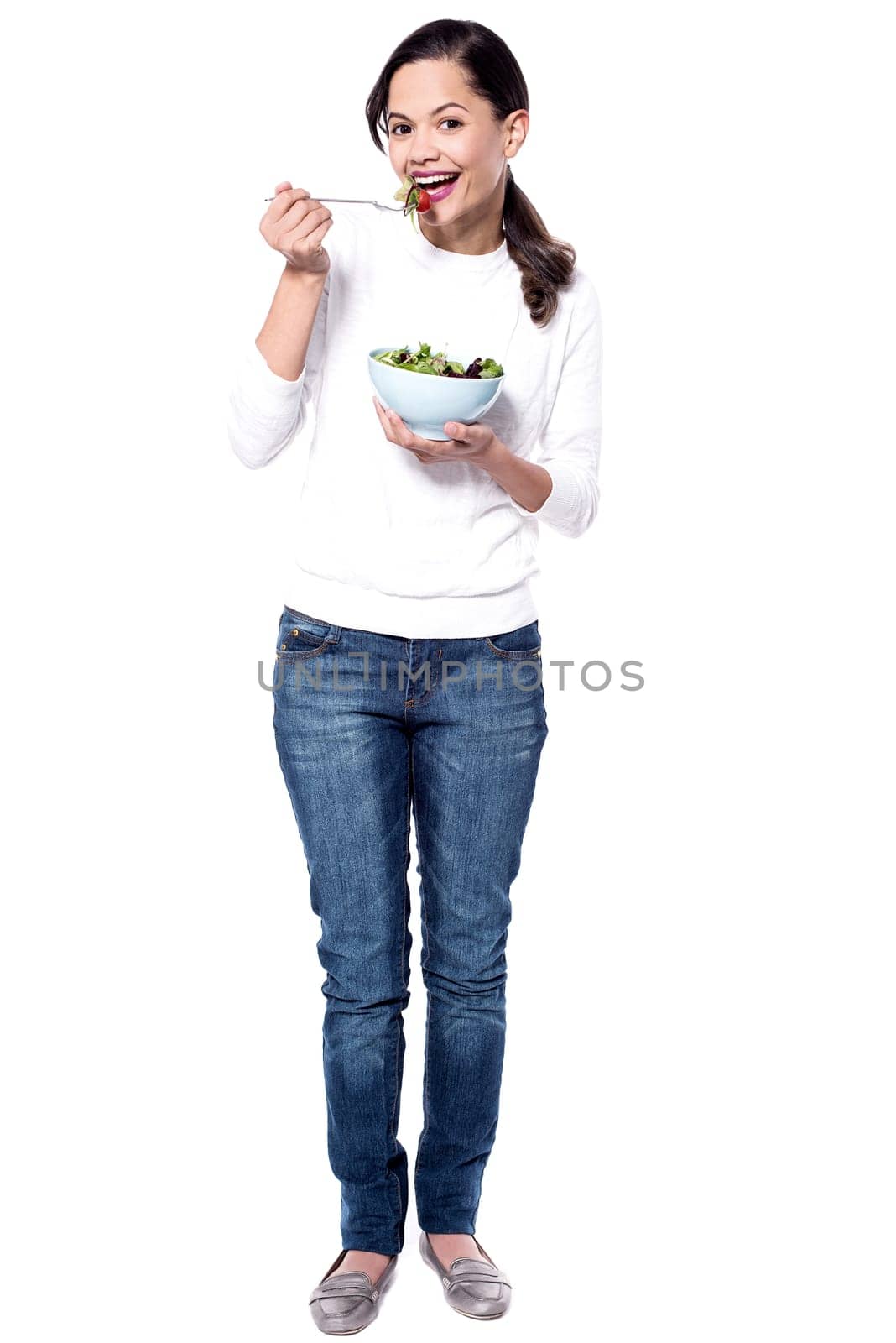 Full image of a young woman eating leafy green salad