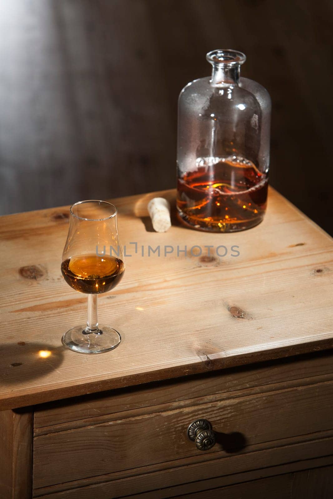 Bottle and a glass of brandy on a vintage wooden table with closed drawer