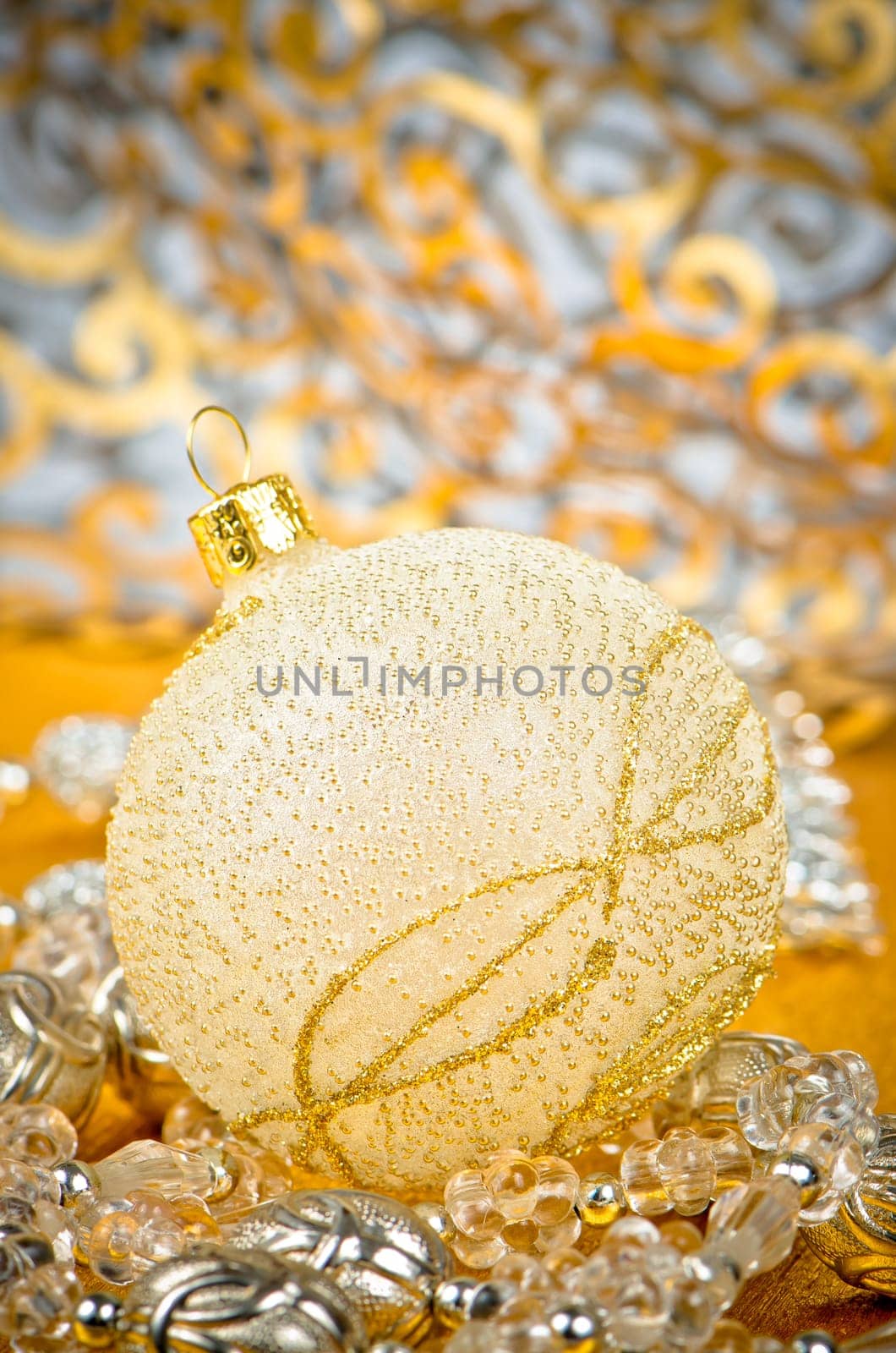 Golden christmas ball with decorations on golden surface and blured backdrop.