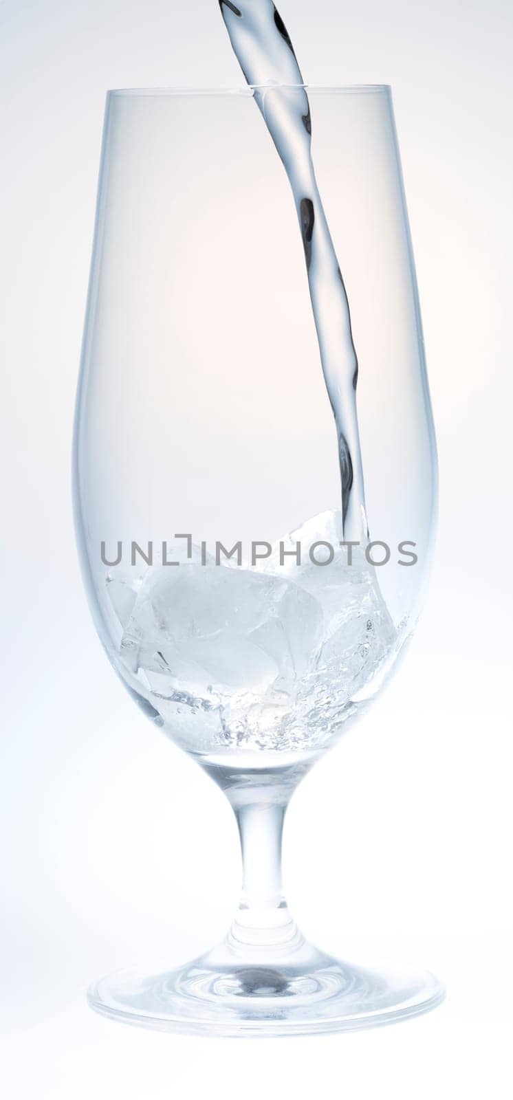 Water Pouring into Glass with Ice on white and grey background.