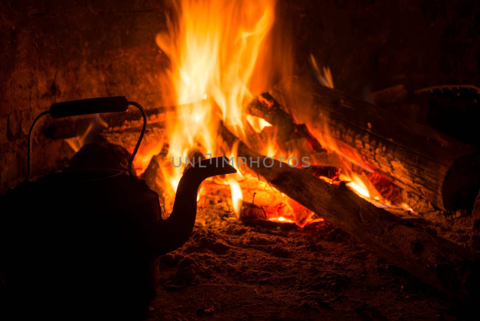 Winter time holiday scene with logs in old rustic fireplace burning and kettle.