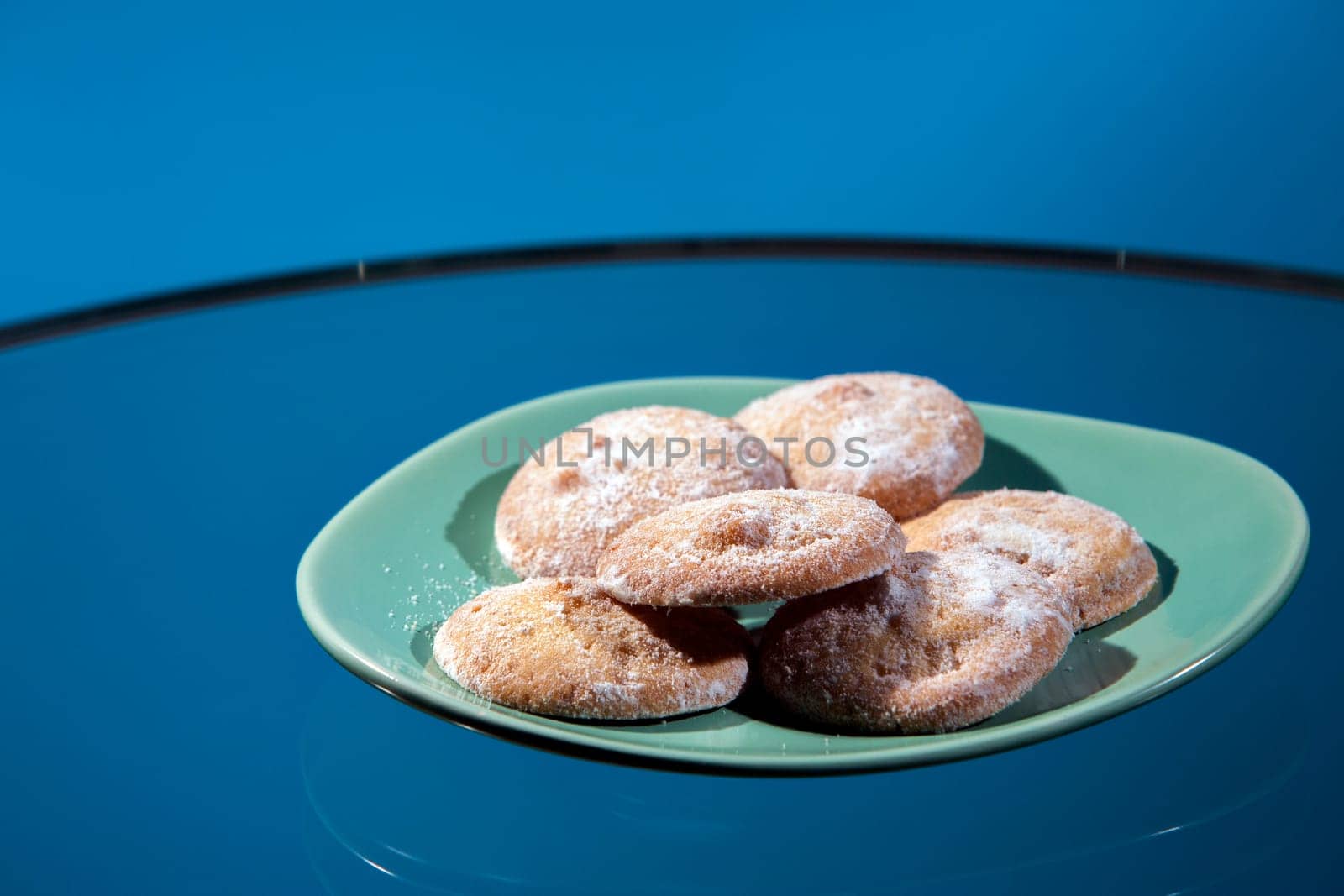Butter lemon cookies on a green retro plate on a glass table with a blue background.