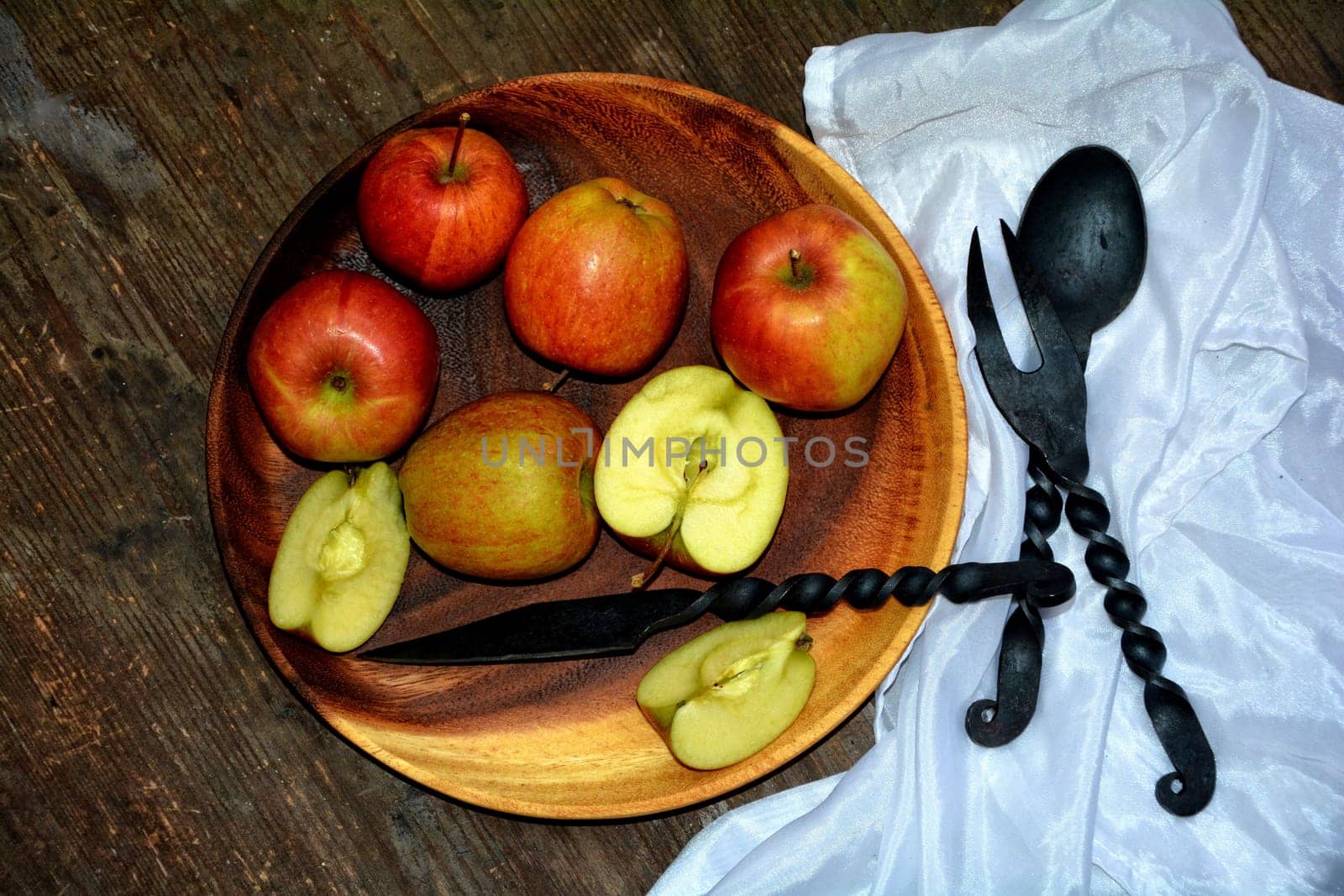 Apples on wooden plate with iron knife,spoon and fork next to it