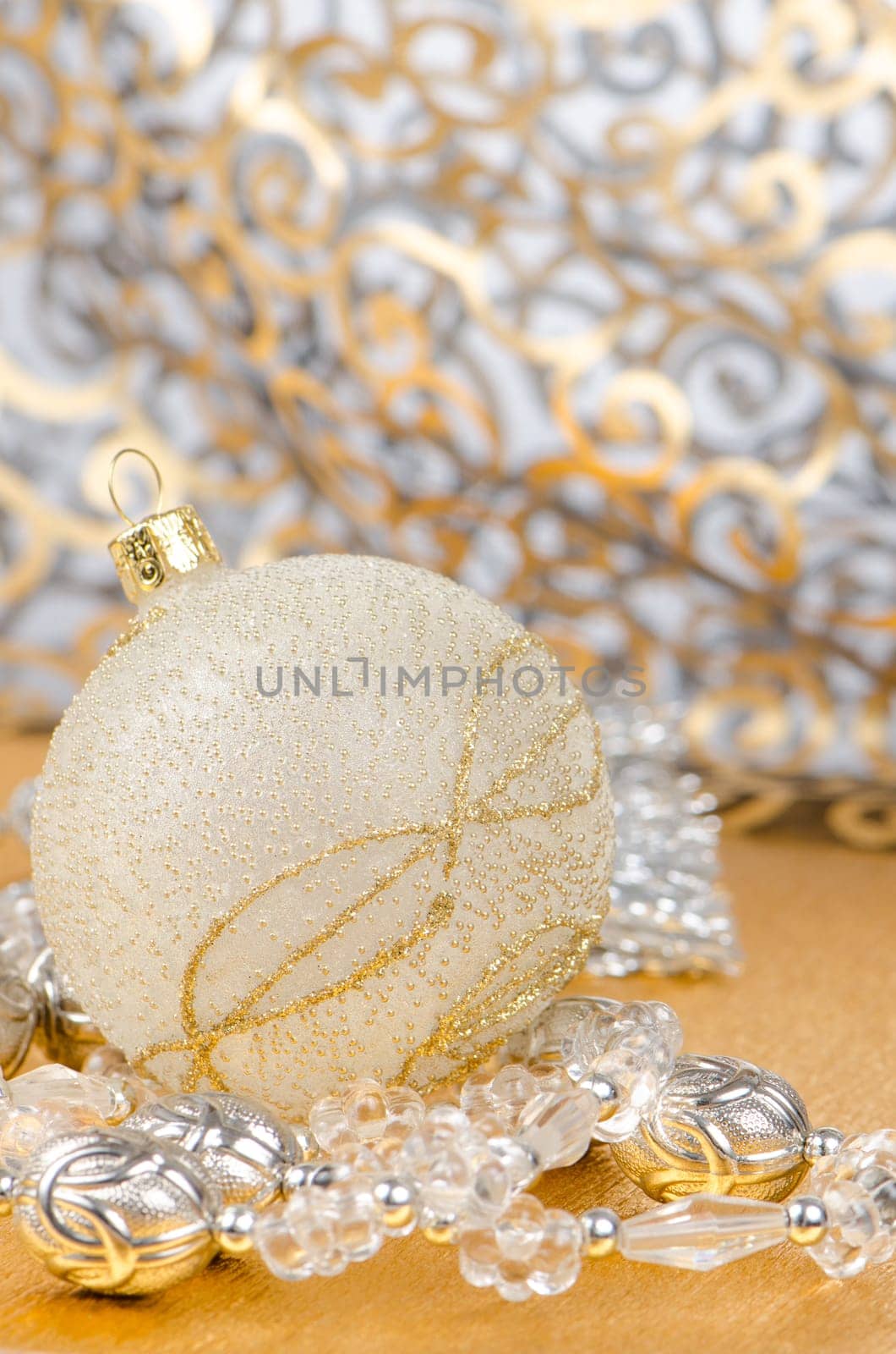 Golden christmas ball with decorations on golden surface and blured backdrop.