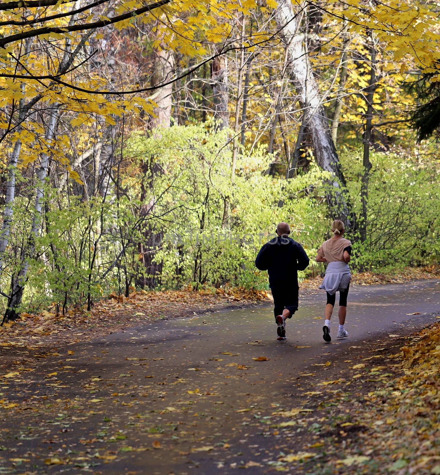 Man and woman running in the autumn forest on the way