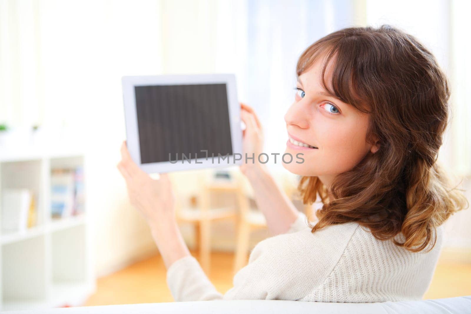 View of a young smiling woman using a tablet on a sofa