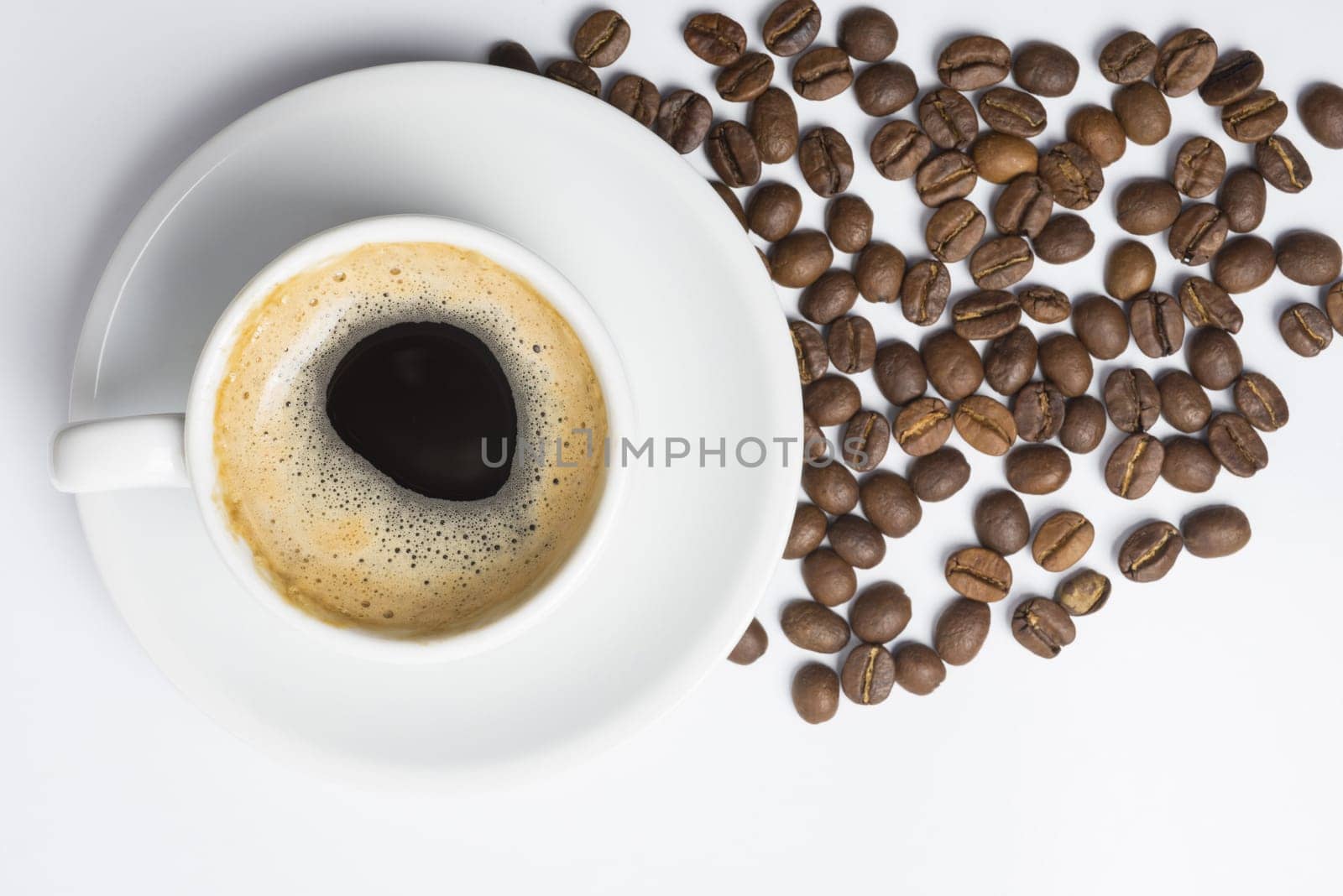 Classic cup of coffee with foam and scattered roasted beans, top view angle. Clipping path included, so you can easily copy and paste it on your own design.