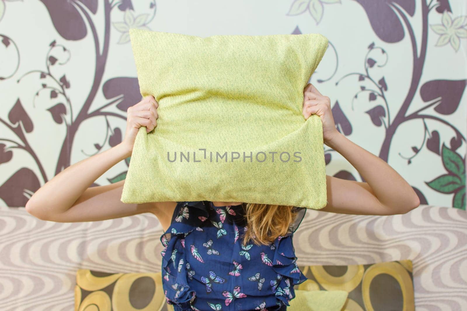 girl hiding behind a green pillow sitting in the living room sofa