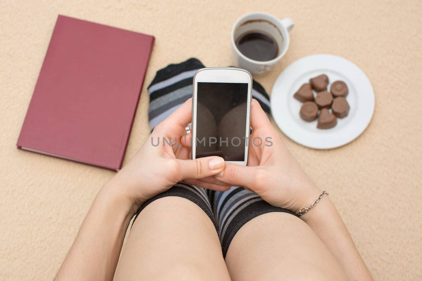 Girl using her phone in bed surrounded by book coffee and dessert