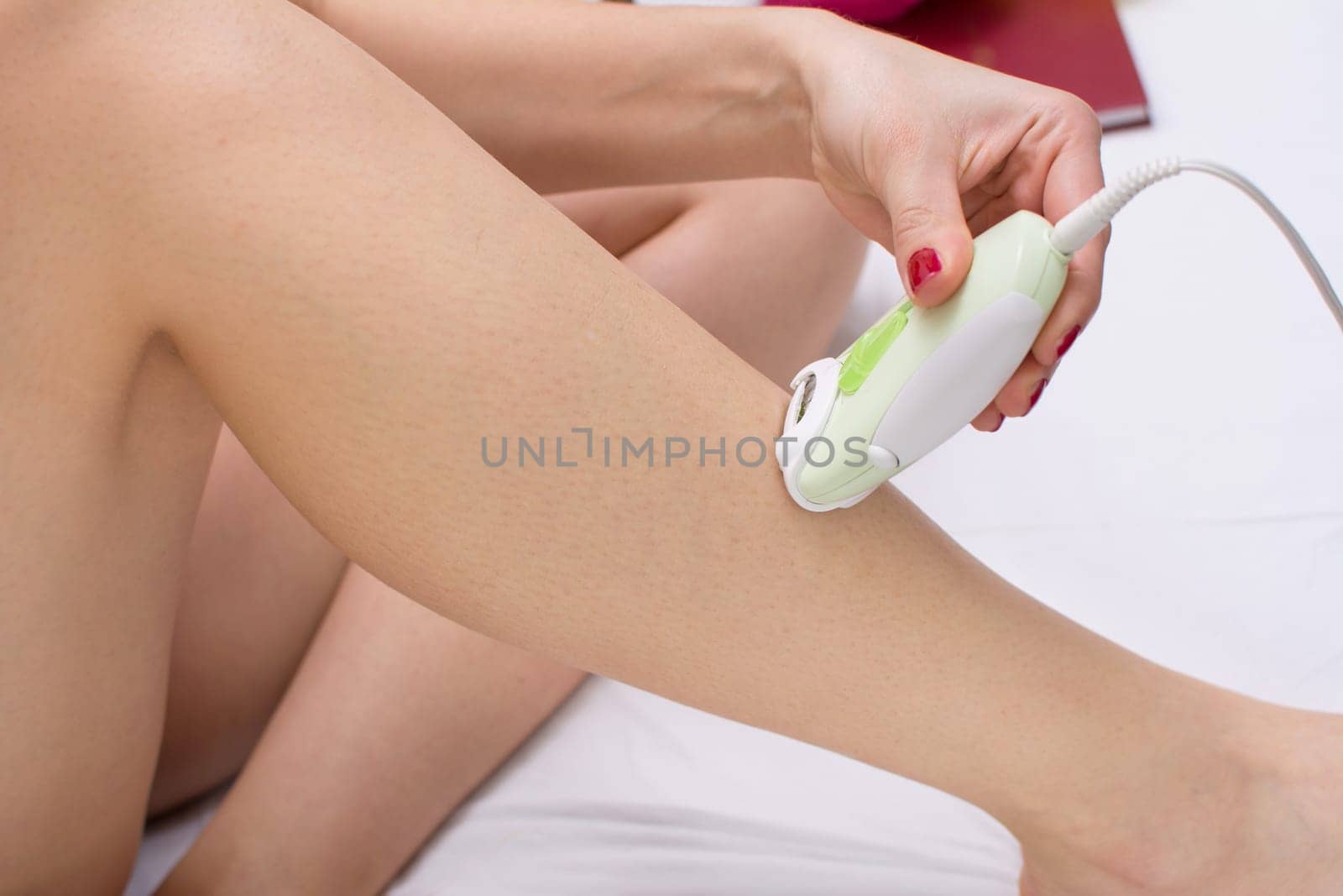 Girl epilates her leg with an epilator on the bed