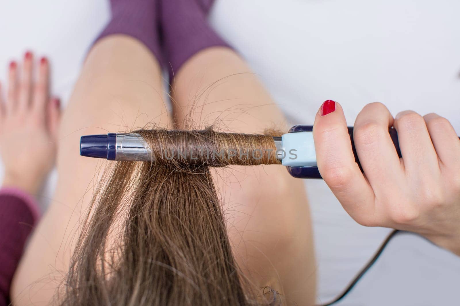 Top view of a girl straightening her hair while sitting in bed