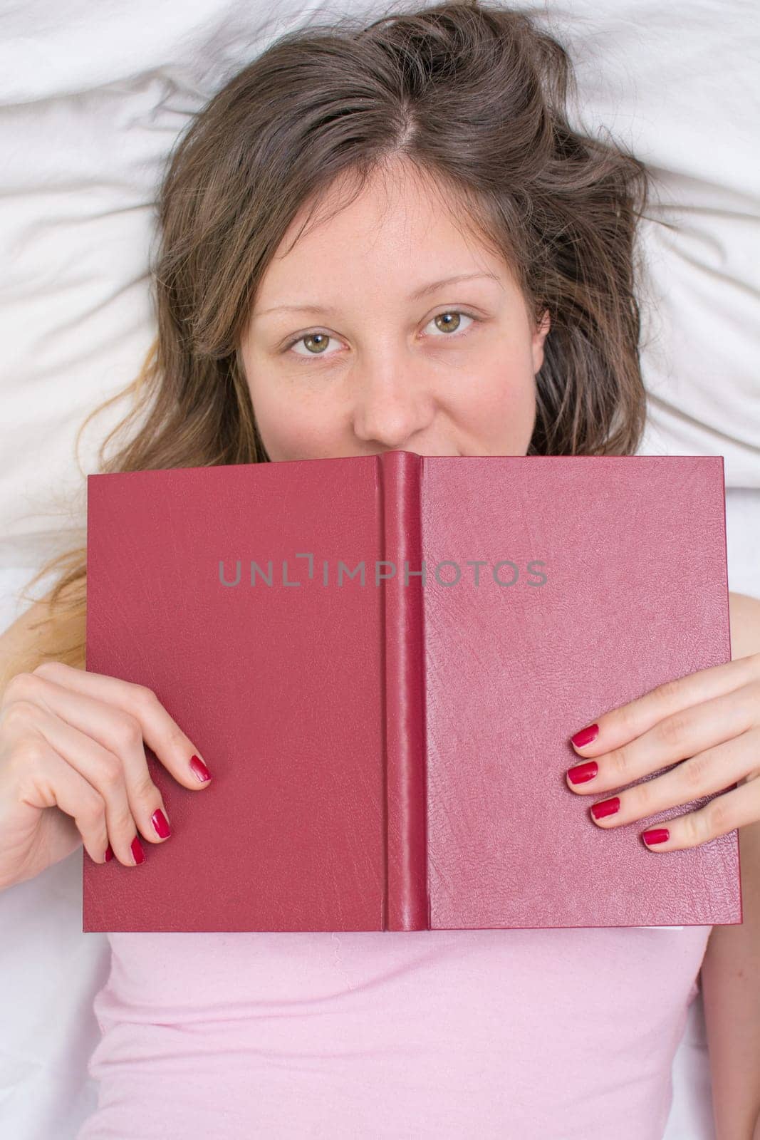 Sleepy girl laying in a bed with a book in her hands