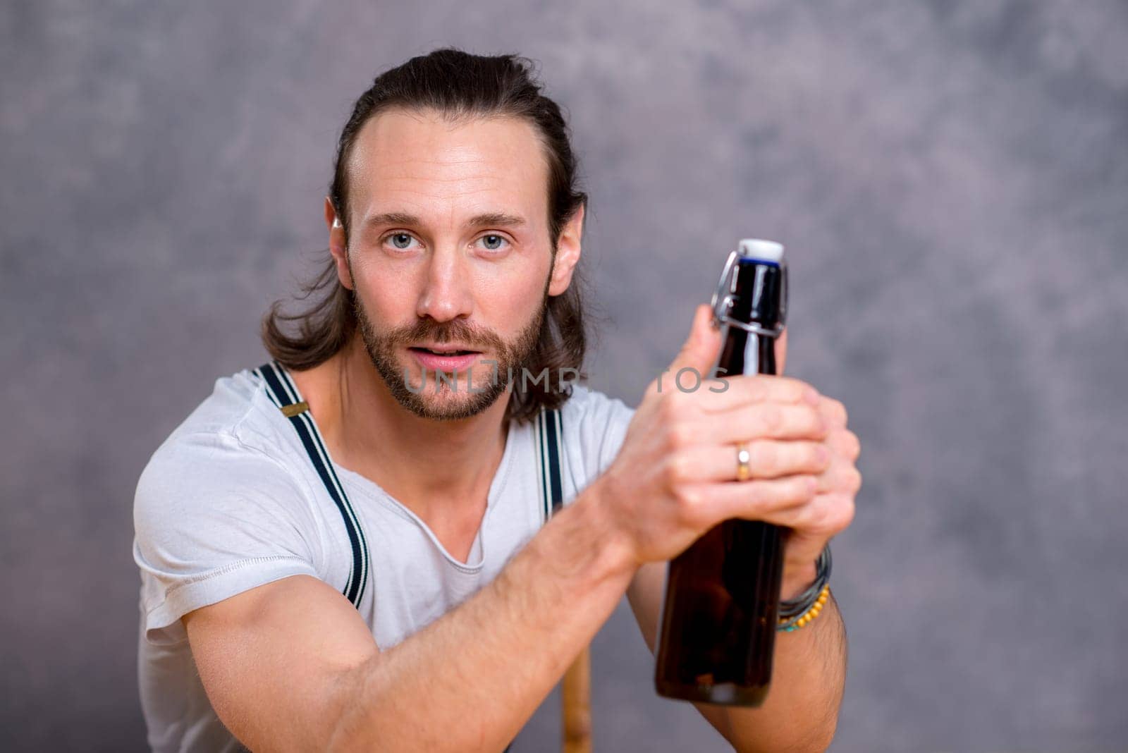 young man in front of gray background opening a beer bottle