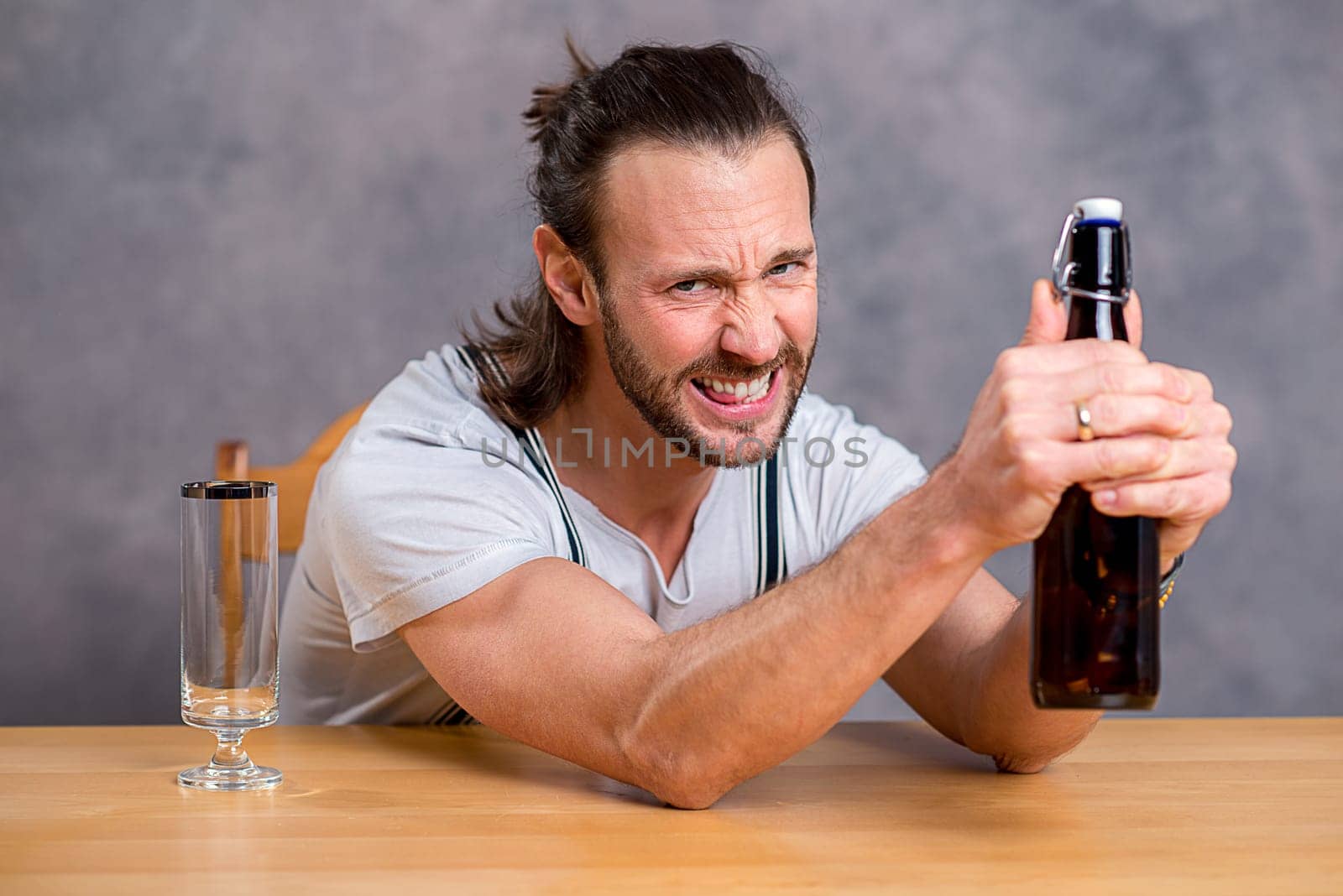 young man in front of gray background opening a beer bottle