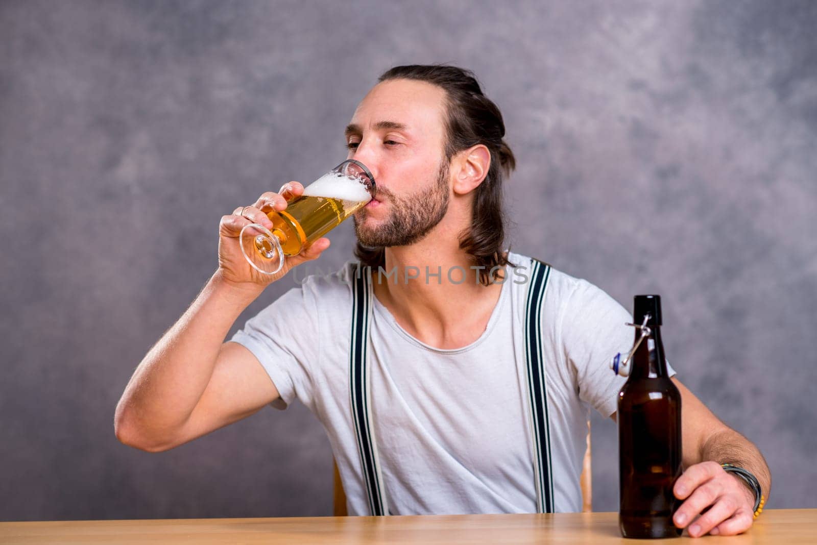 young man in front of gray background drinking beer
